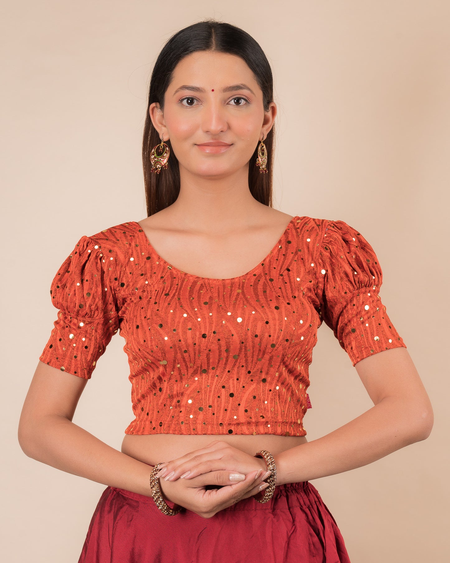 Model wearing a red stretchable blouse with gold mirror embellishments, puff sleeves, and round neckline