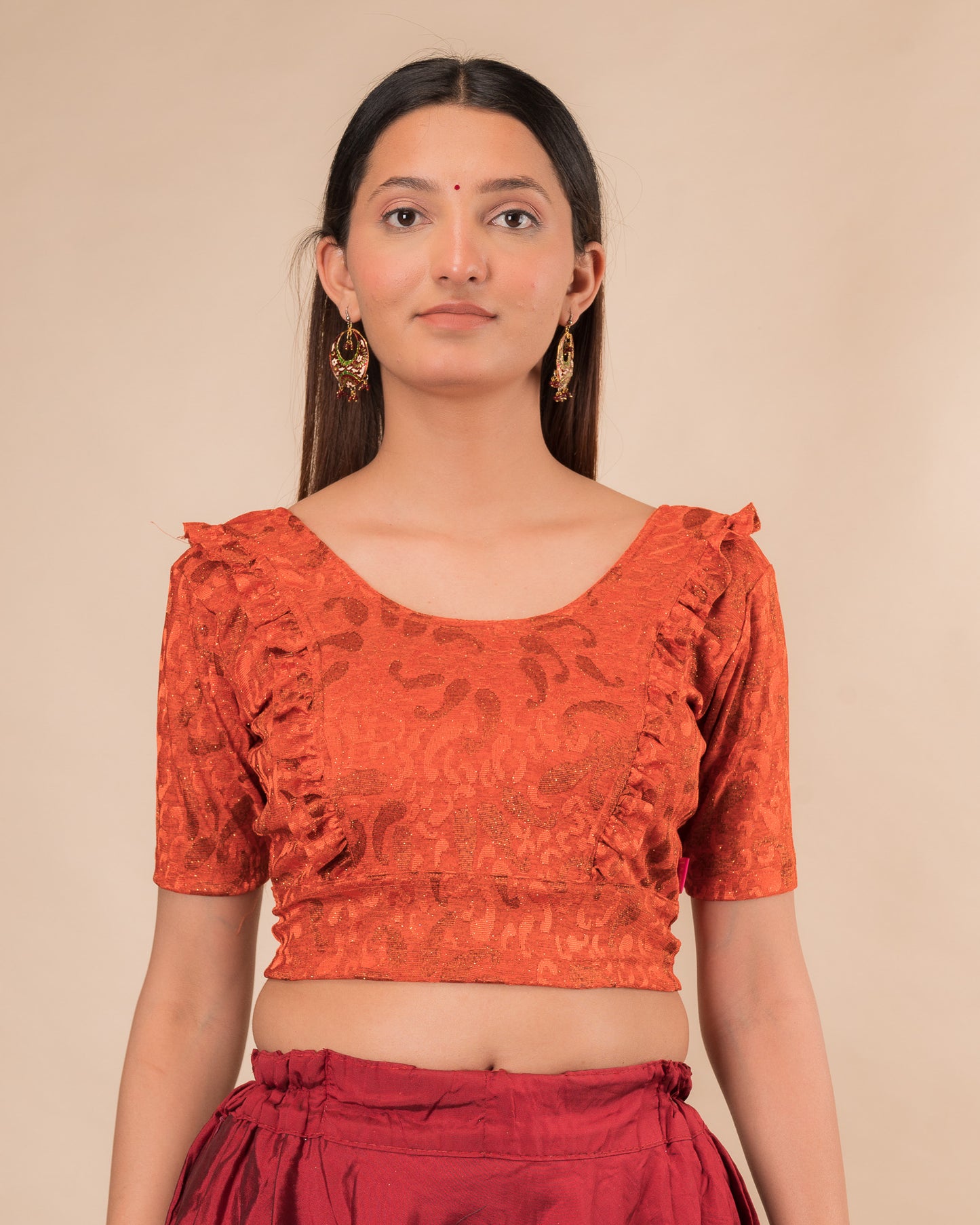 Model wearing an orange paisley paisley stretchable blouse with glitter, ruffled shoulders, elbow sleeves, and round neckline