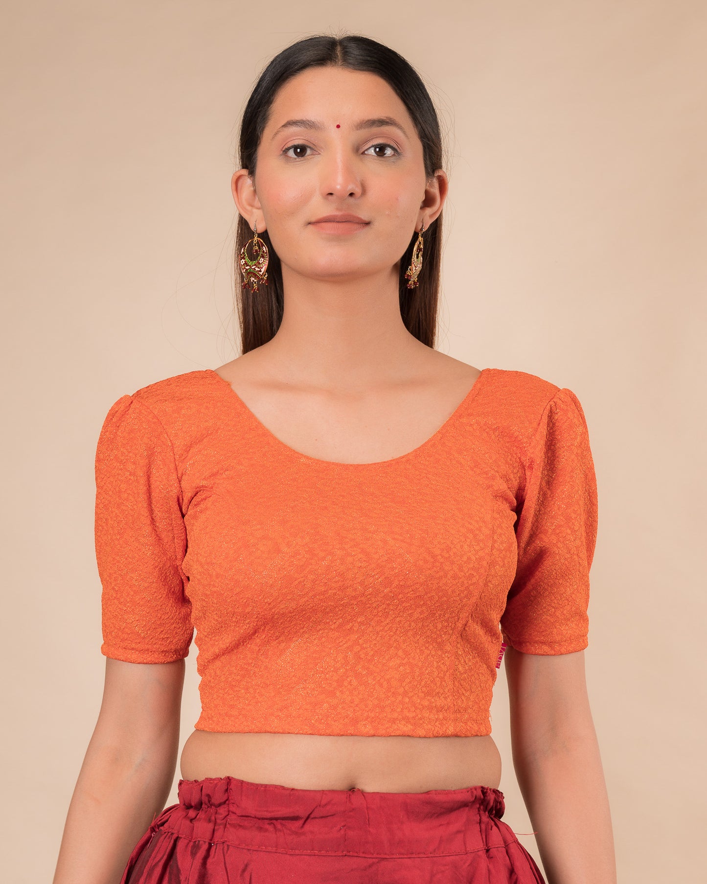 Model wearing an orange paisley paisley stretchable blouse with glitter, ruffled shoulders, elbow sleeves, and round neckline