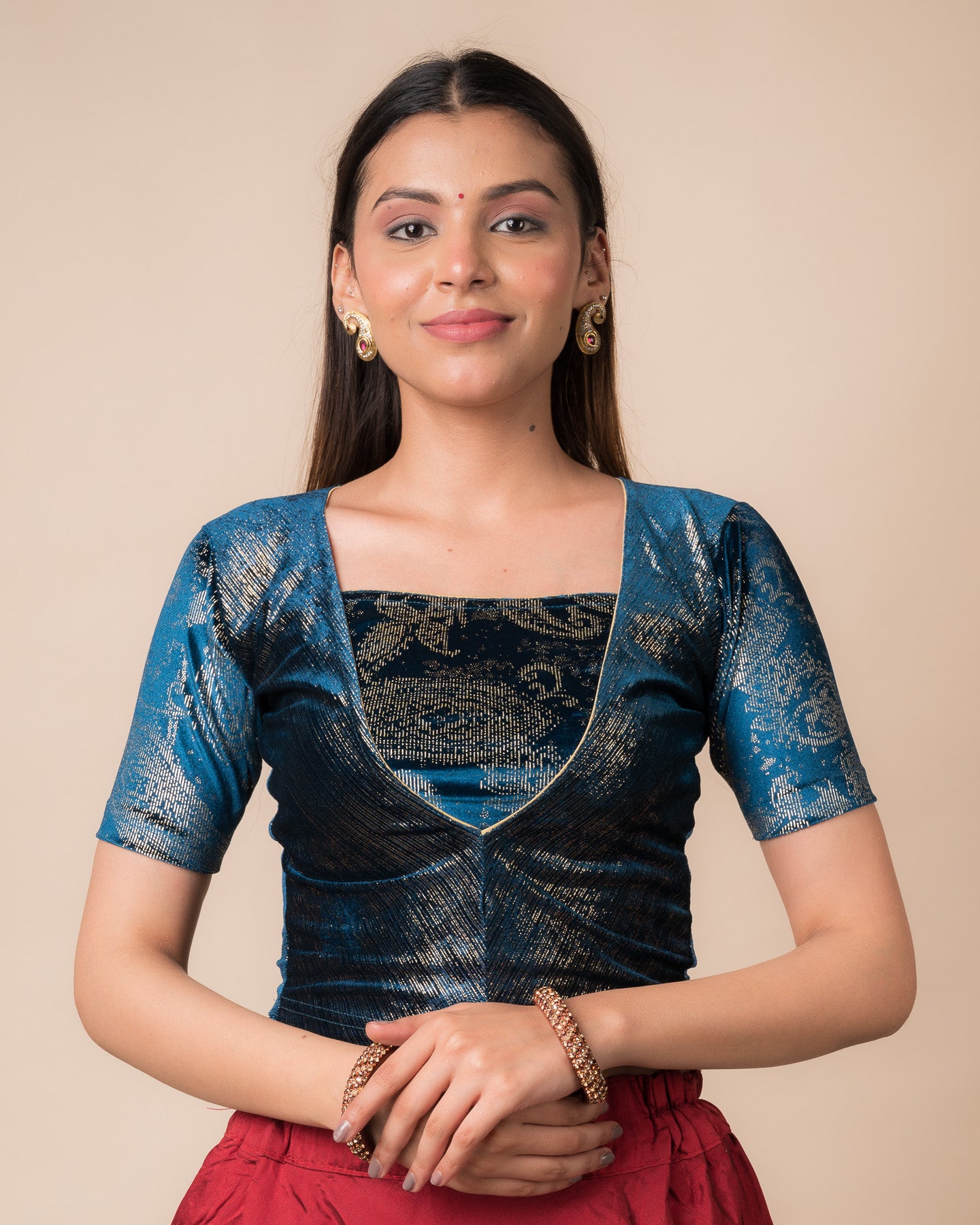 Model wearing a teal blue-colored velvet embellished stretchable choli-style readymade blouse with elbow sleeves and round neckline.