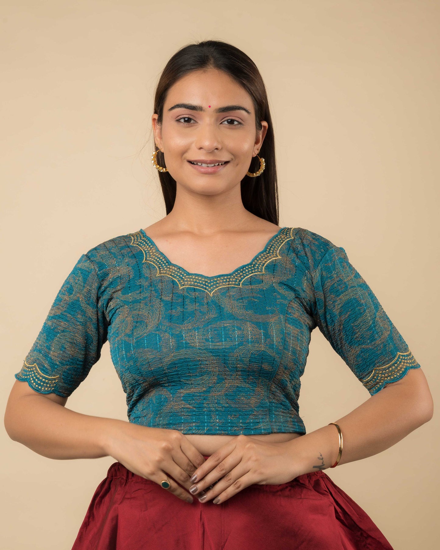 Model wearing a rama green-colored stretchable readymade blouse with zari embroidery, elbow sleeves, and scalloped round neckline.