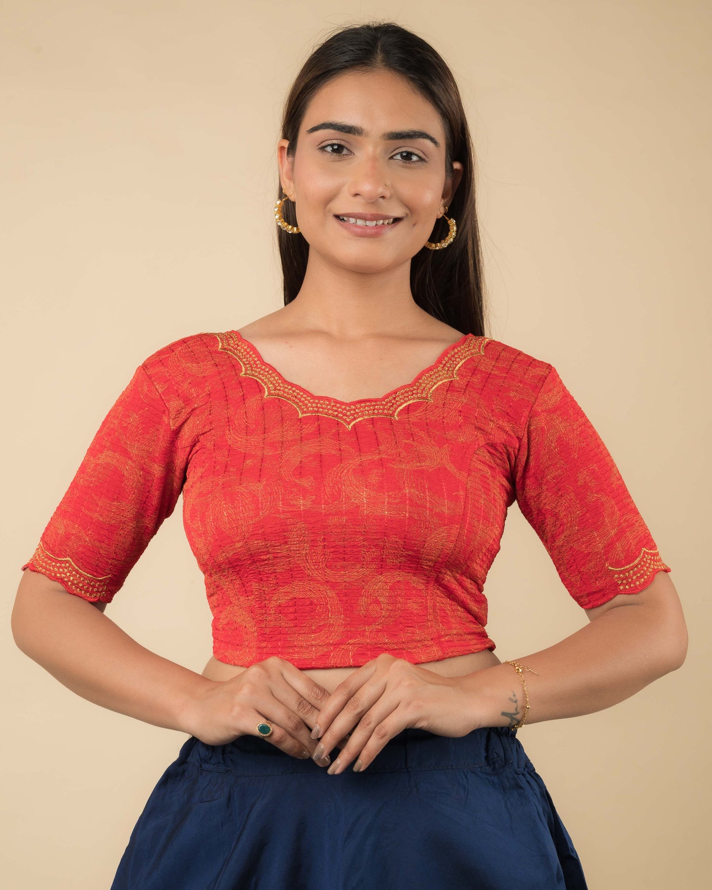 Model wearing a red-colored stretchable readymade blouse with zari embroidery, elbow sleeves, and scalloped round neckline.