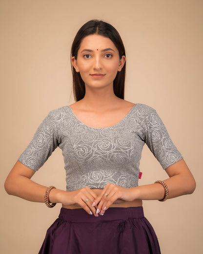 Model wearing a stretchable blouse with elbow sleeves and round neckline, featuring metallic emboss detailing.