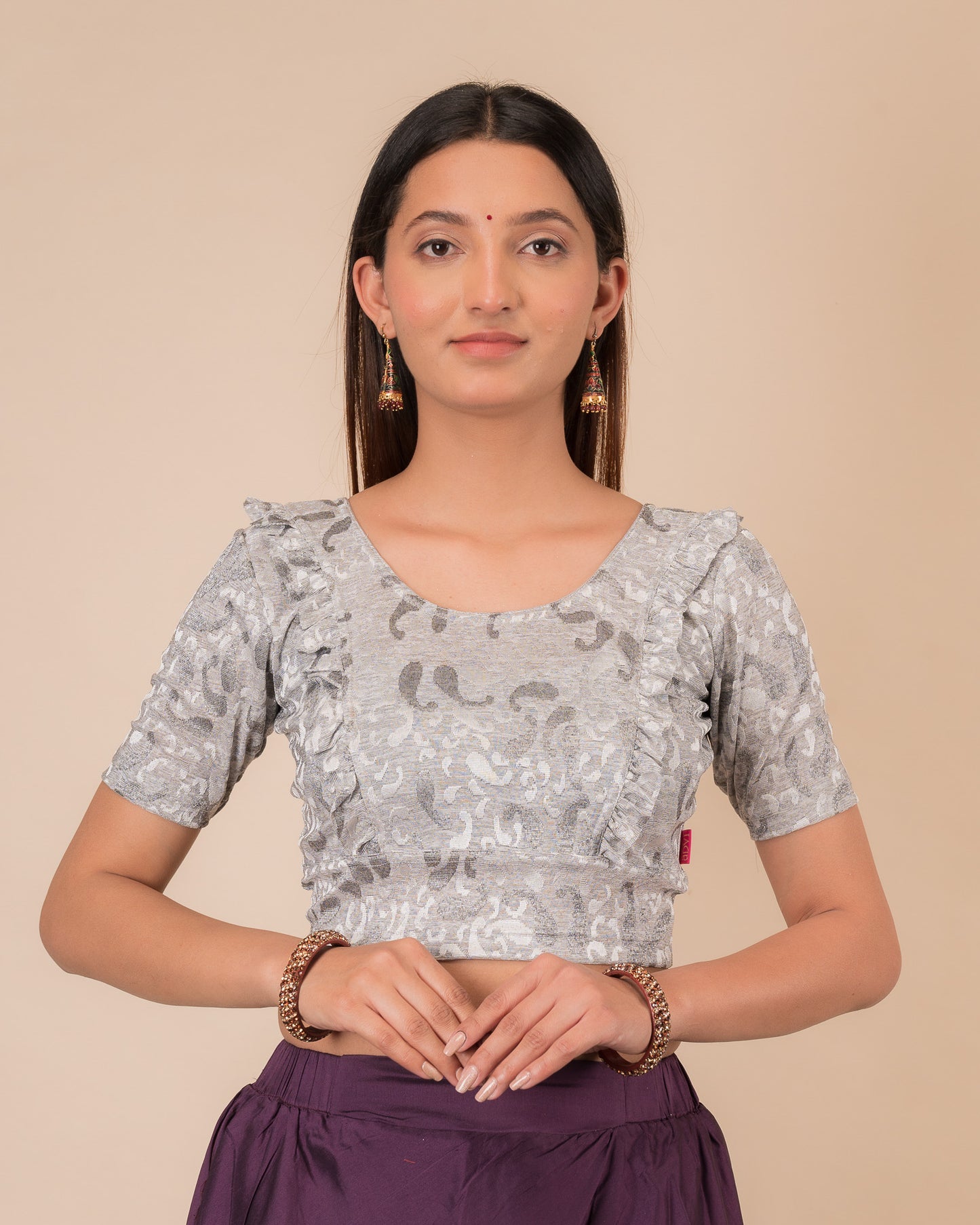 Model wearing an orange paisley paisley stretchable blouse with glitter, ruffled shoulders, elbow sleeves, and round neckline