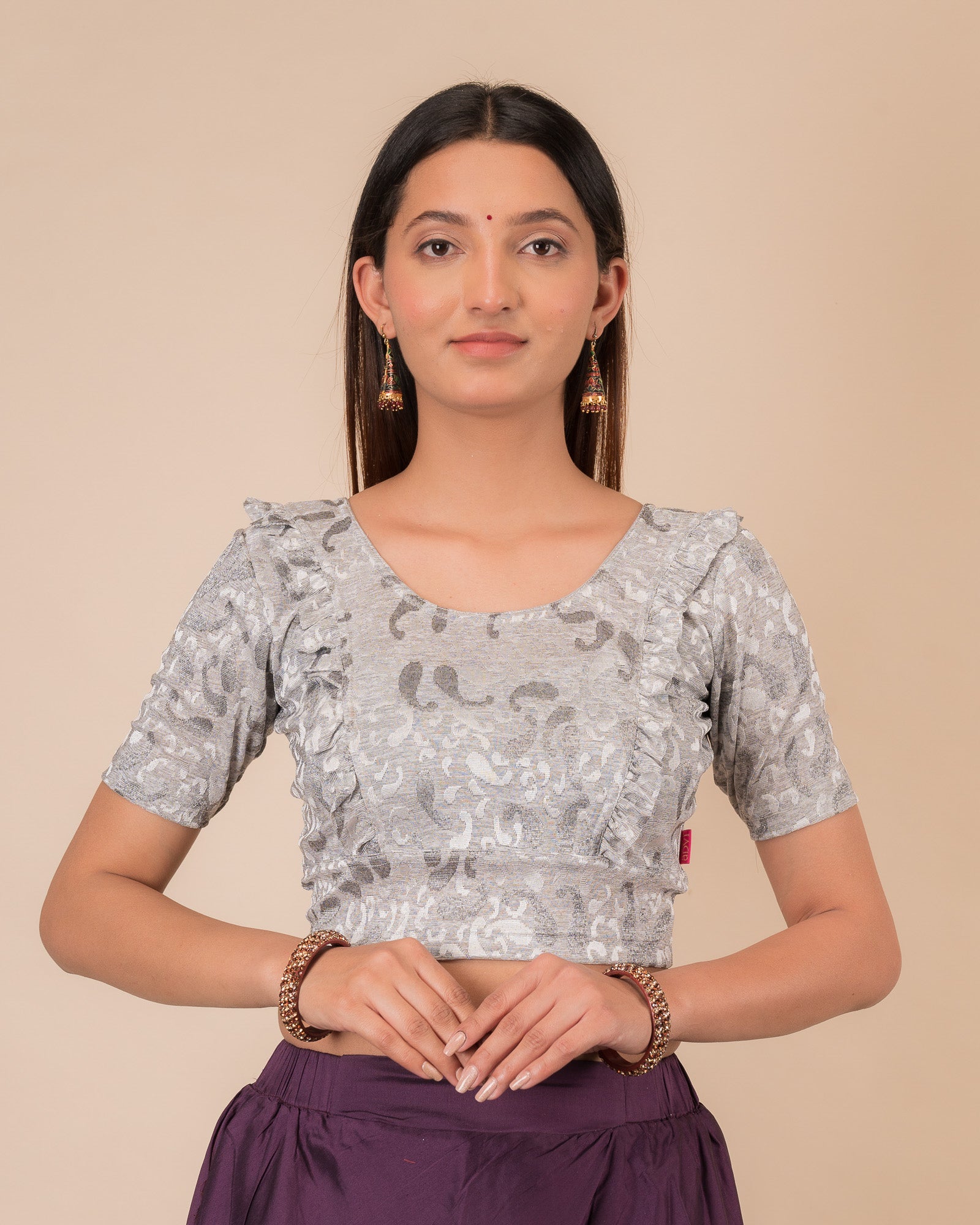 Model wearing an orange paisley paisley stretchable blouse with glitter, ruffled shoulders, elbow sleeves, and round neckline