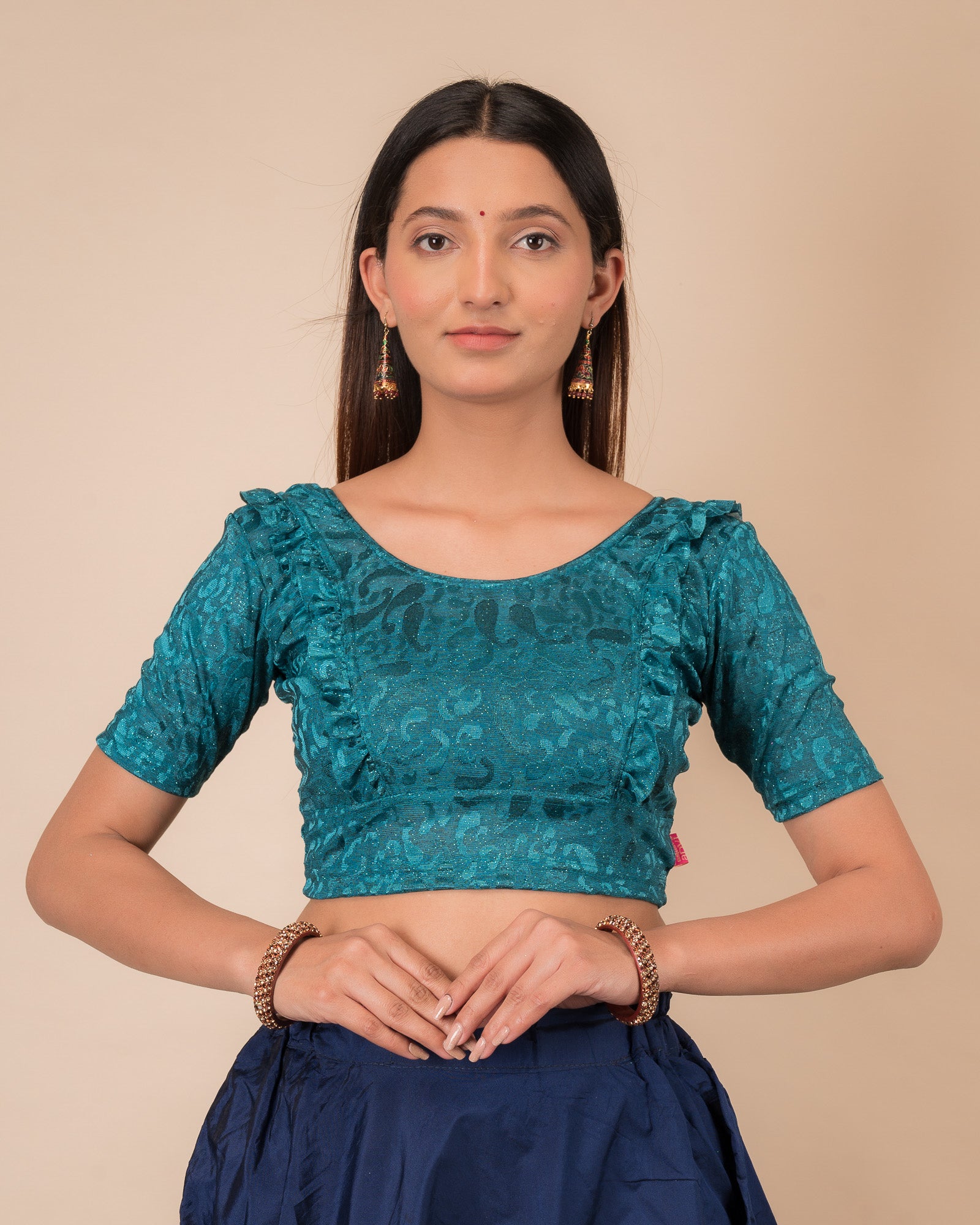 Model wearing an orange paisley paisley stretchable blouse with glitter, ruffled shoulders, elbow sleeves, and round neckline