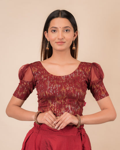 Model wearing a stretchable foil-textured blouse with sheer puff sleeves and round neckline