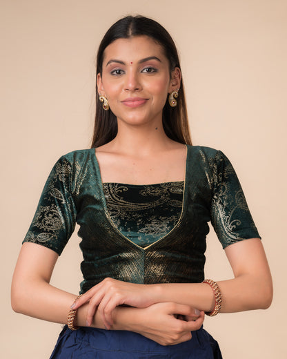 Model wearing a bottle green-colored velvet embellished stretchable choli-style readymade blouse with elbow sleeves and round neckline.