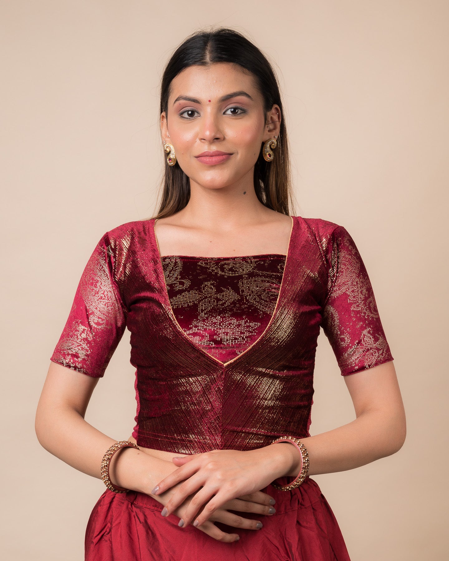 Model wearing a maroon-colored velvet embellished stretchable choli-style readymade blouse with elbow sleeves and round neckline.
