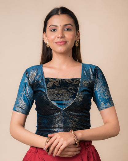 Model wearing a teal blue-colored velvet embellished stretchable choli-style readymade blouse with elbow sleeves and round neckline.