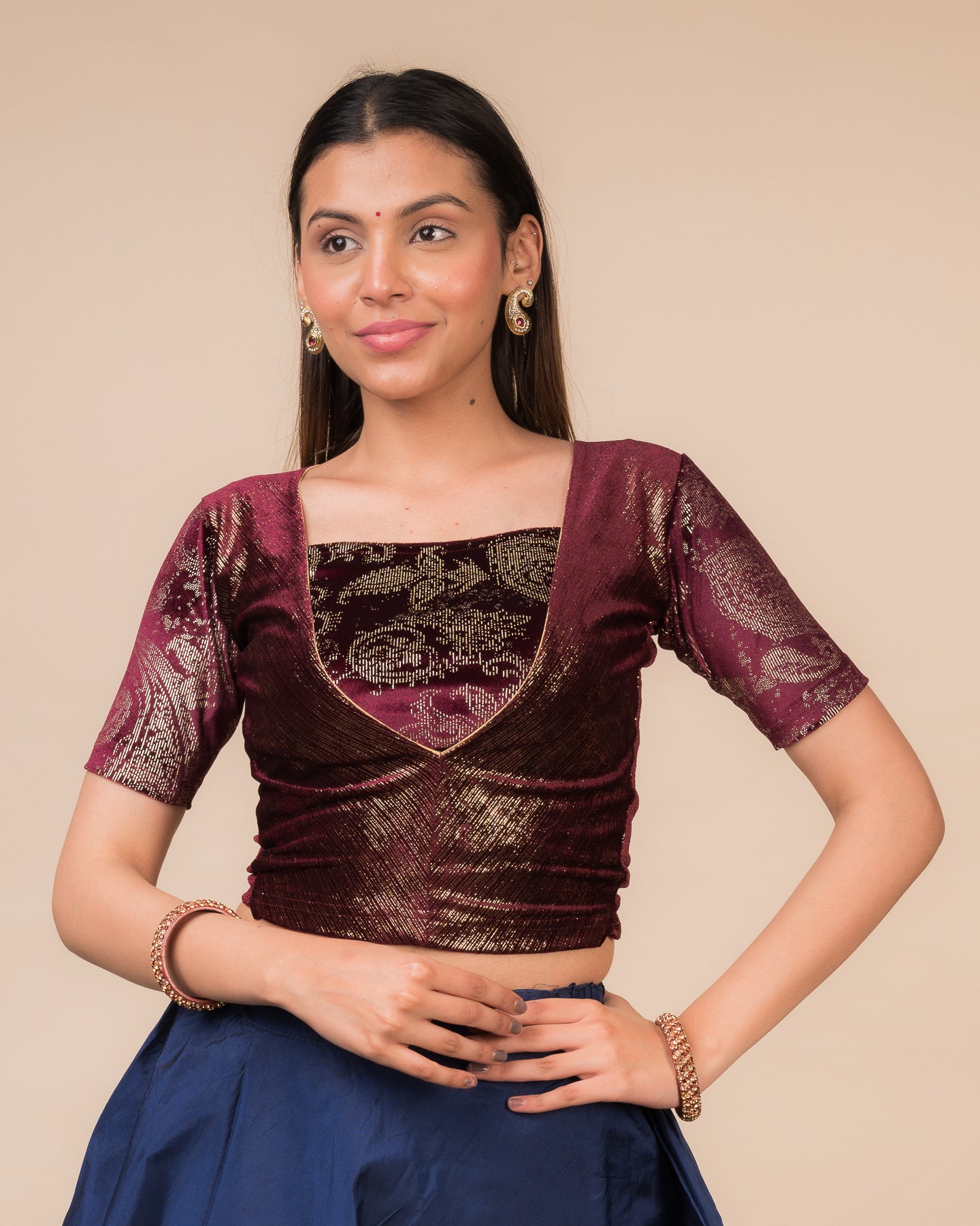 Model wearing a wine-colored velvet embellished stretchable choli-style readymade blouse with elbow sleeves and round neckline.