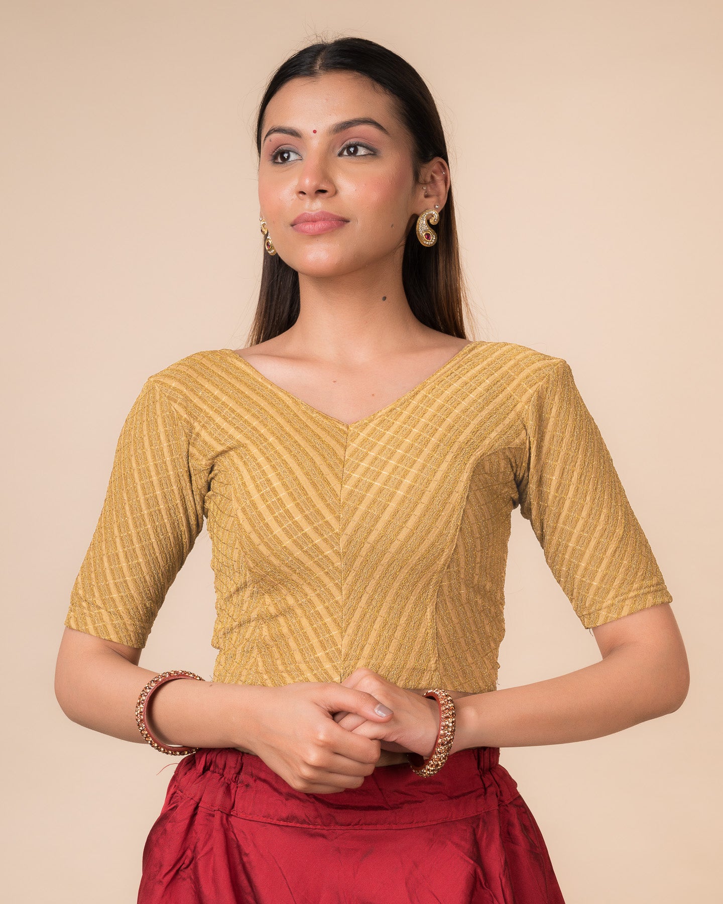Model wearing a beige gold zari stretchable readymade blouse with elbow sleeves and V-neckline.